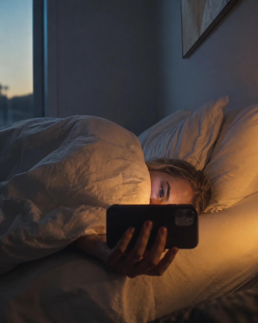 Scrolling in bed at first light, face lit by the phone